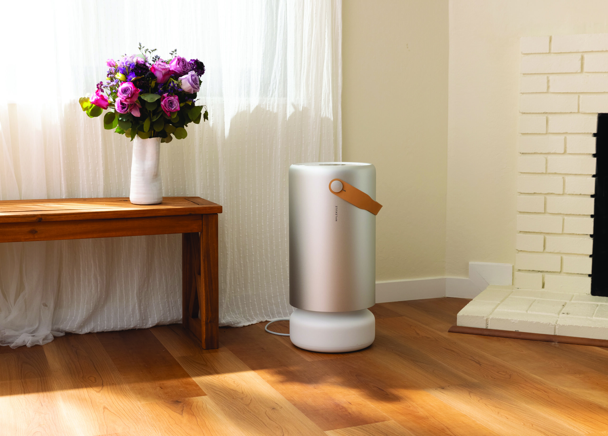 A modern living room featuring the Molekule Pro Air purifier placed beside a window with natural light and hardwood floors.