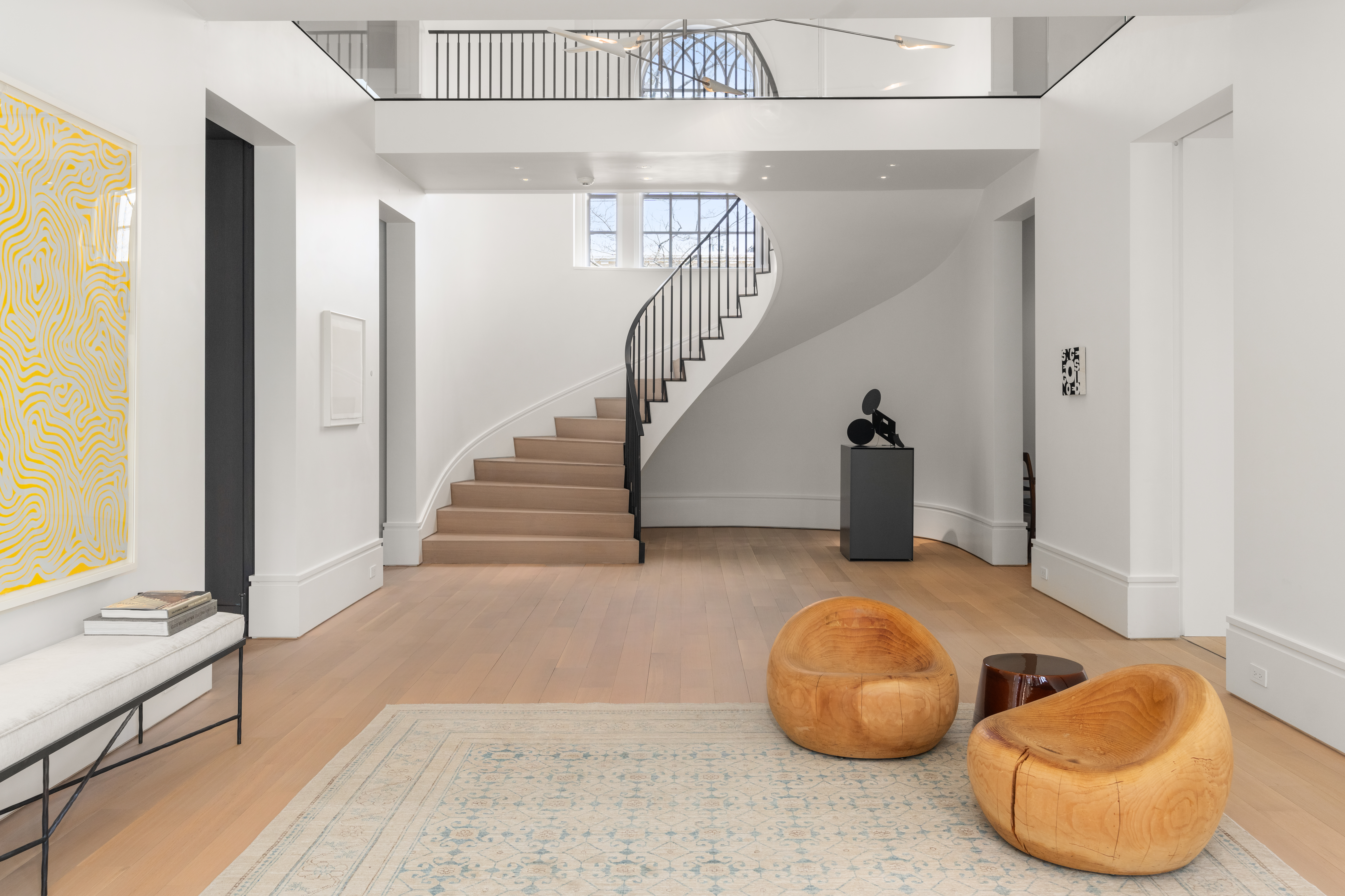 Modern interior entryway featuring a curved staircase, light wood floors, minimalist decor, and contemporary art in a West Cambridge luxury home.