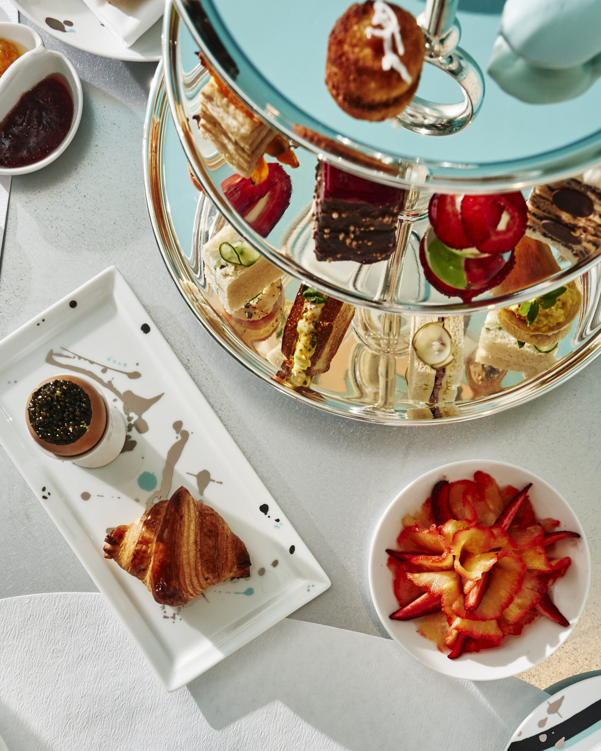 Elegant high-tea spread at Blue Box Café with tiered trays of pastries, croissants, desserts, and fresh berries displayed on Tiffany-blue tableware.